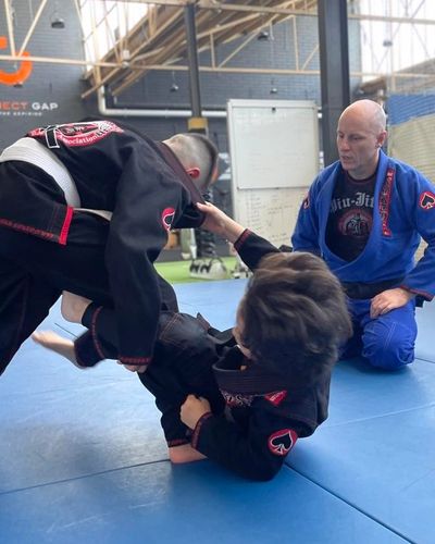 Two people practicing Brazilian Jiu-Jitsu with an instructor observing.
