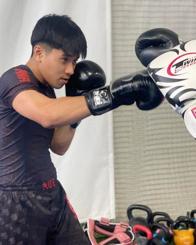 A young man practicing boxing with gloves in a gym.