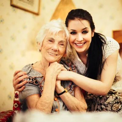 A young woman embraces an elderly woman with a warm smile indoors.