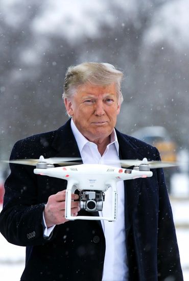 A man in a coat holding a flying drone in a snowy outdoor setting.