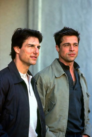 Tom Cruise and Brad Pitt standing side by side outdoors, looking ahead.