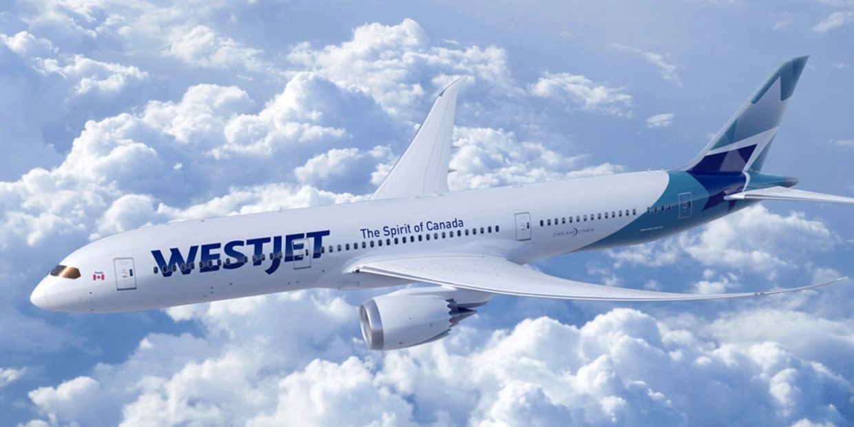 A WestJet airplane flying above the clouds with clear blue skies.