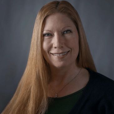 Smiling woman with long red hair against a dark background.