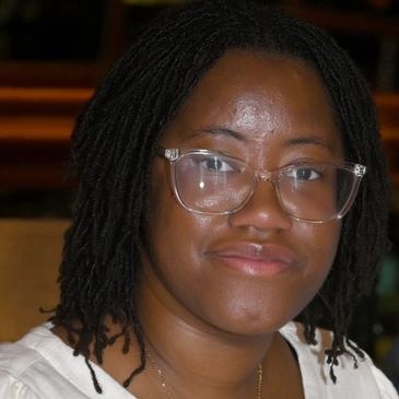 Smiling woman with glasses and dreadlocks.