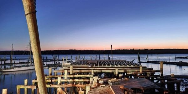 Wooden dock under construction at sunset over calm water.