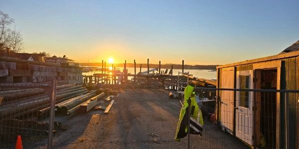 Sunset over a construction site near a waterfront with pipes and a small building.