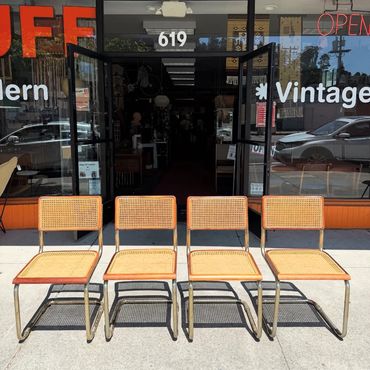 Four vintage cane chairs lined up outside a store with glass doors.