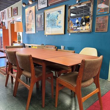 Mid-century wooden table and chairs in a cozy, art-filled room.