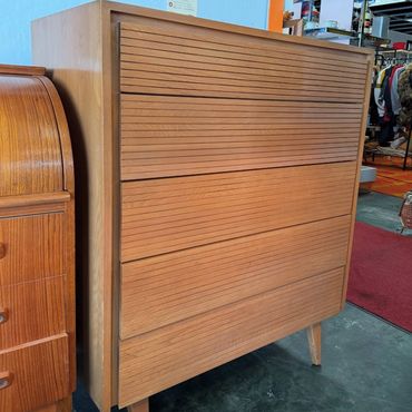 Mid-century modern wooden dresser with horizontal grooves and tapered legs.