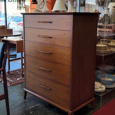 Mid-century wooden dresser with five drawers and sleek handles in a vintage store.