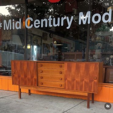 Mid-century modern wooden sideboard with drawers and cabinets outside a store.