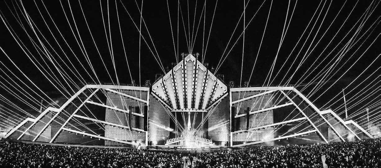 Black and white image of a concert stage with lights and a large crowd.