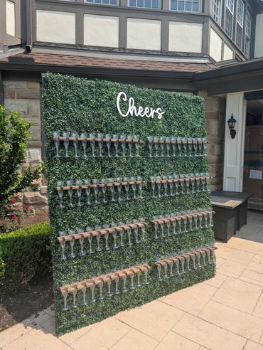 Decorative wall with empty champagne glasses and 'Cheers' sign outdoors.