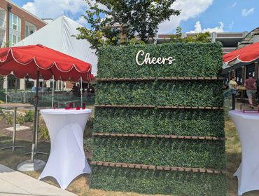 Outdoor event setup with a greenery wall and red umbrellas.
