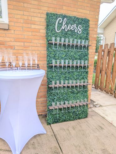 A stylish champagne glass display with a 'Cheers' sign on a greenery backdrop.