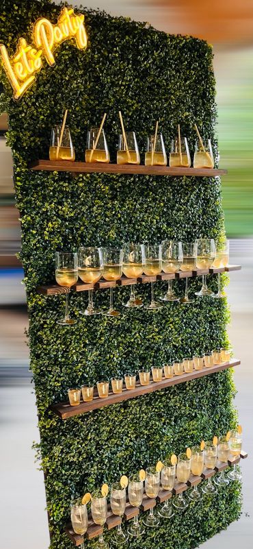 Green party wall with shelves holding various drinks and a glowing 'Let's Party' sign.