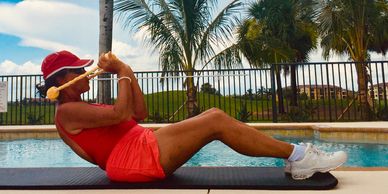 Woman exercising by the pool, drinking from a bottle, wearing red workout clothes.