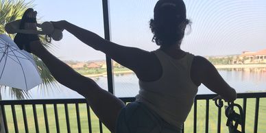 Silhouette of a person stretching leg on a balcony with scenic water view.