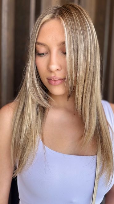 Young woman with blonde hair wearing a light purple top, looking down thoughtfully.