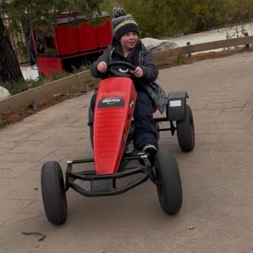 Child riding a red pedal go-kart outdoors.