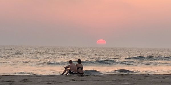 Couple sitting on the beach watching a pink sunset over the ocean.