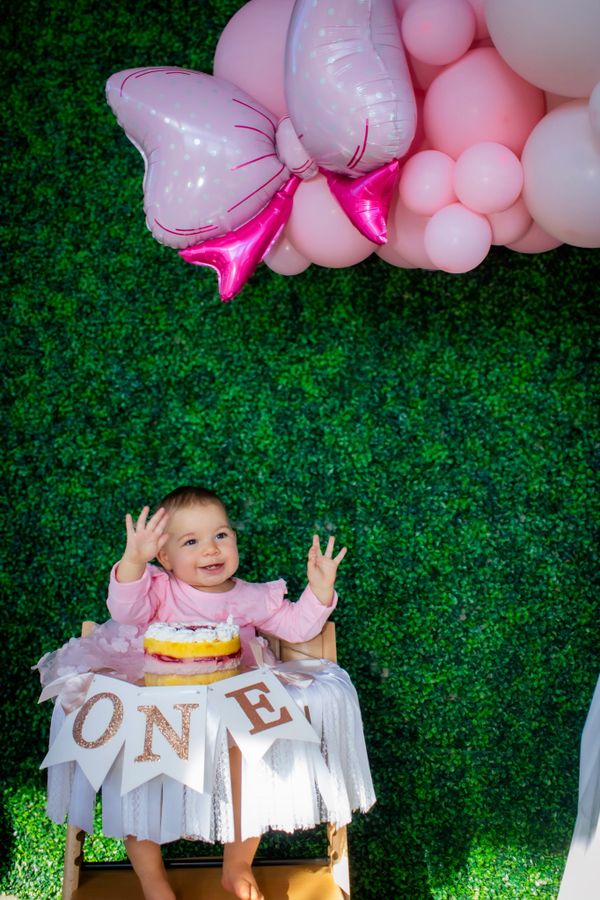 Happy baby celebrating first birthday with cake and pink balloons.