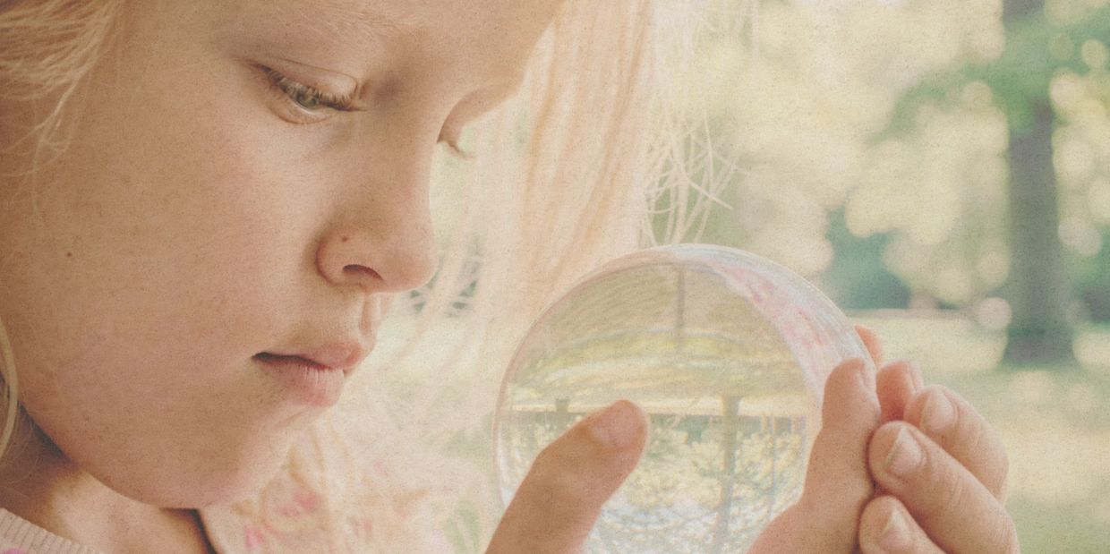 Child closely examining a glass sphere outdoors.