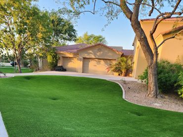 A curved, lush artificial turf installation by Tempe Turf Installers in front of a home at dusk.
