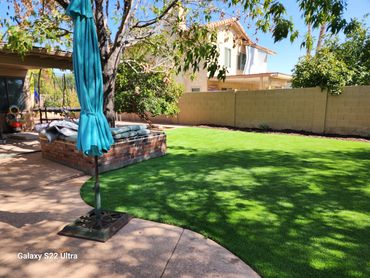 A patio with folded umbrella, artificial grass installed by Tempe Turf Installers, and a tree.