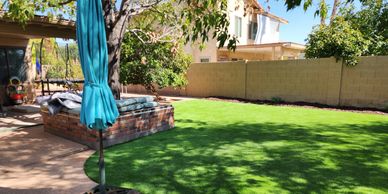 Arizona backyard with turf, blue umbrella, and stone patio