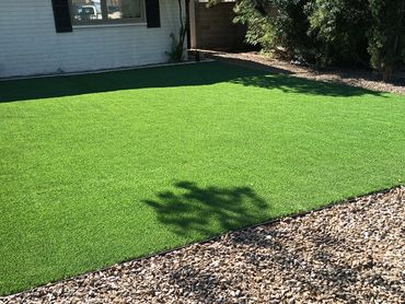 A home with trees, a rock bed and an artificial turf installation by Tempe Turf Installers.