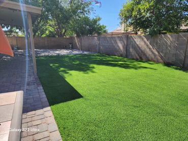 A sunny backyard with an artificial grass installation by Tempe Turf Installers with a patio area.