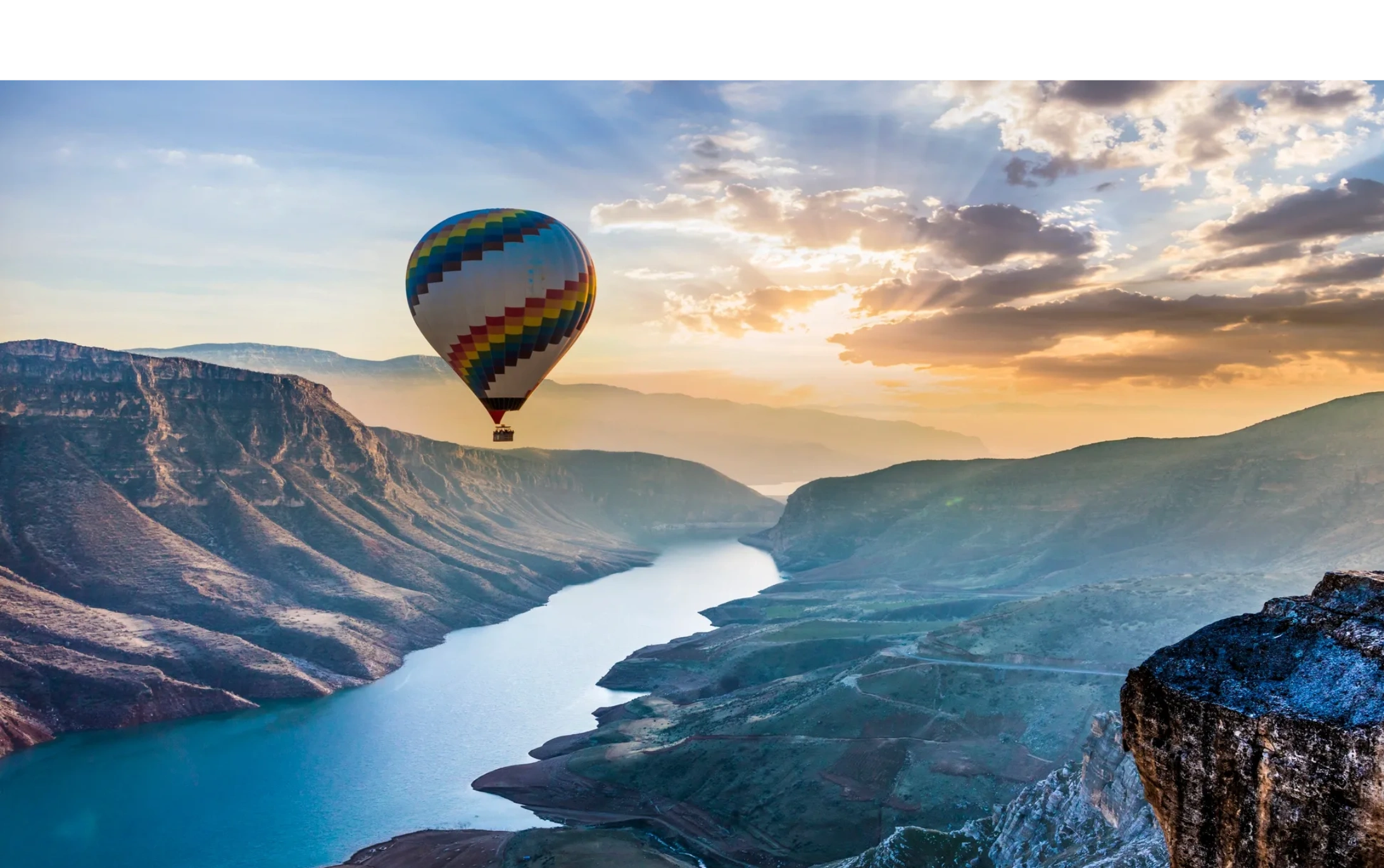 Hot air balloon floating over a river canyon at sunrise.