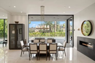 Modern dining room with large windows overlooking a pool and greenery.