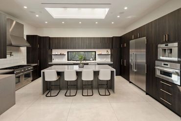 Modern kitchen with dark wood cabinets and a large island with white chairs.
