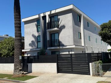 Modern three-story apartment building with black balconies and a black fence.