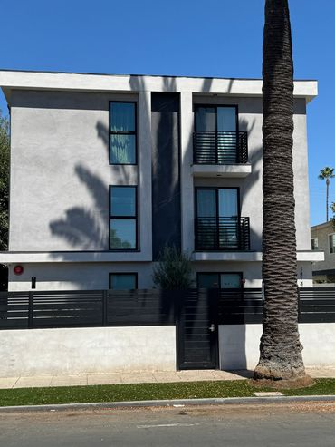 Modern three-story building with black balconies and palm tree shadows.