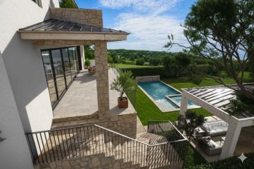 Modern house with stone exterior, a pool, and outdoor seating area under a pergola.
