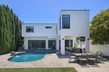 Modern white house with a pool and outdoor dining area under a clear blue sky.