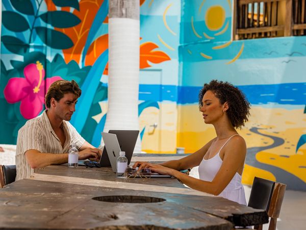 Two people working on laptops at a colorful outdoor cafe table.