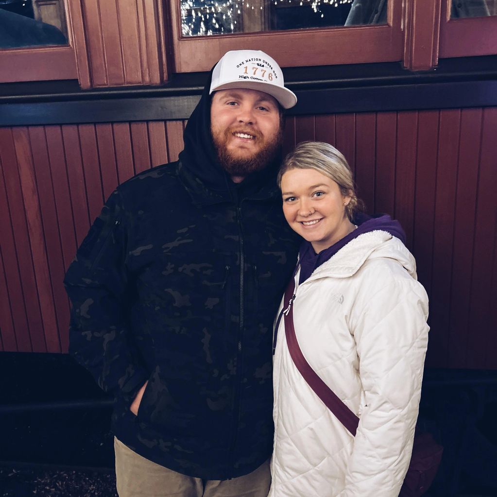 Smiling couple in warm jackets posing indoors against a wooden wall.