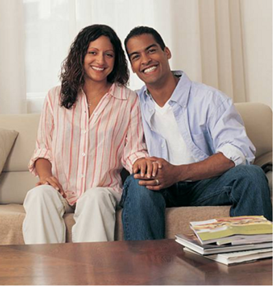 Smiling couple sitting together on a couch holding hands.