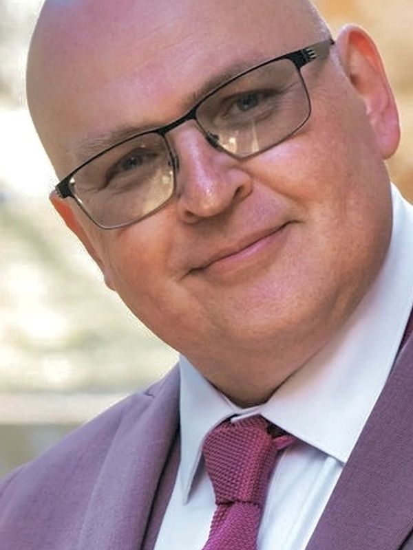 Smiling bald man wearing glasses, a suit, and a tie.