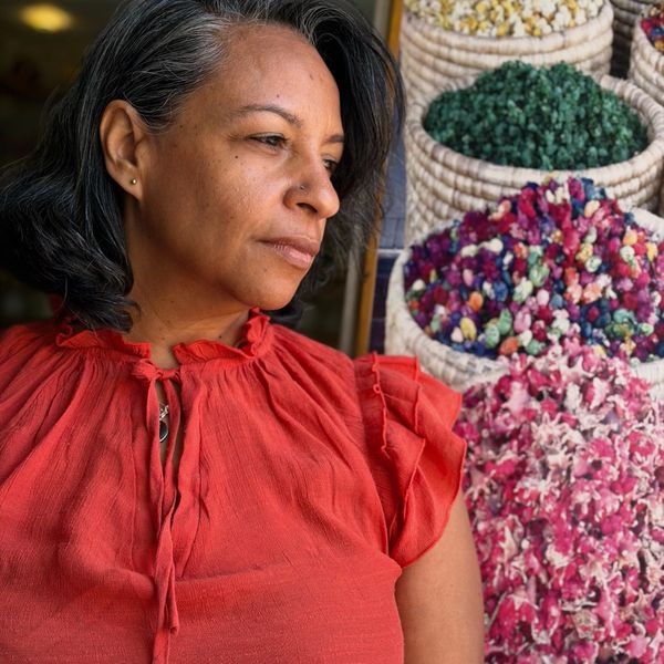Woman in a red blouse stands near baskets filled with colorful dried flowers.