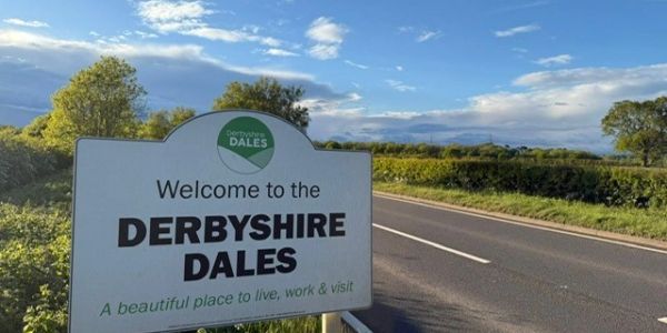Welcome sign for the scenic Derbyshire Dales by a country road.