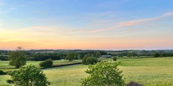 Peaceful countryside landscape at sunset with green fields and trees.