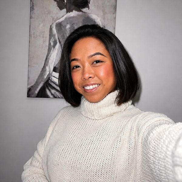A woman in a white turtleneck sweater smiling indoors.