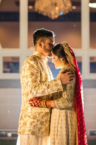 A groom tenderly kisses the bride's forehead in a glowing embrace.