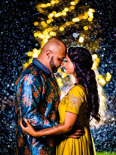 A couple embraces under glowing lights and raindrops at night.
