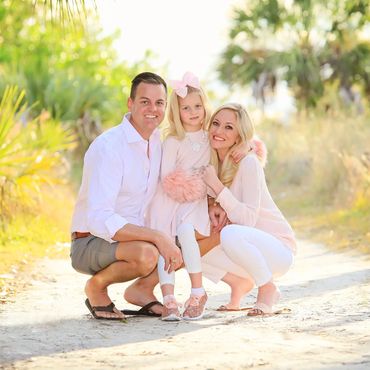 Smiling family of three posing outdoors on a sunny day.
